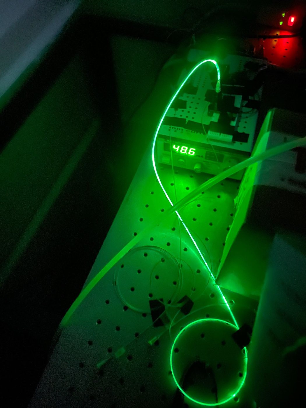 Glowing green fiber optic cable looped across an optical table